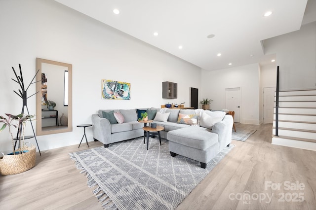 living area with light wood-style floors, recessed lighting, stairway, and a high ceiling