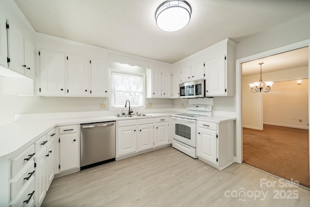 kitchen featuring light wood-style flooring, a sink, appliances with stainless steel finishes, white cabinetry, and a notable chandelier