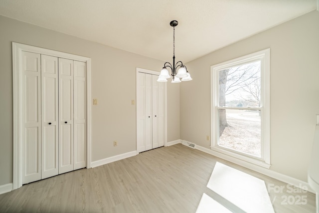 unfurnished dining area featuring light wood-type flooring, an inviting chandelier, visible vents, and baseboards