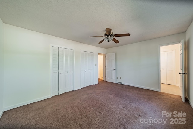 unfurnished bedroom with baseboards, a ceiling fan, carpet, a textured ceiling, and multiple closets