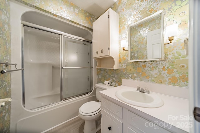 bathroom featuring toilet, shower / bath combination with glass door, vanity, and wallpapered walls