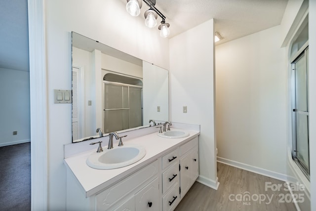 full bath featuring double vanity, a shower stall, a sink, and wood finished floors