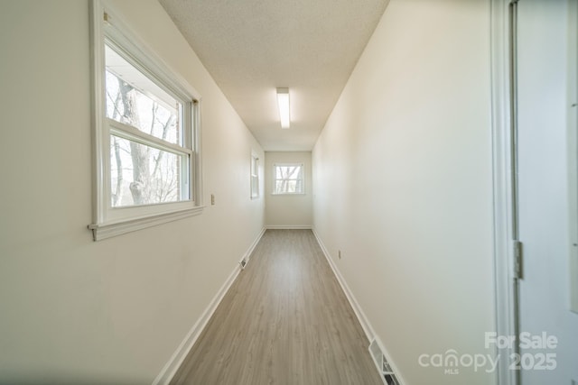 corridor featuring a textured ceiling, wood finished floors, visible vents, and baseboards