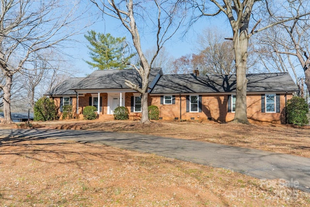 ranch-style house featuring crawl space, brick siding, a chimney, and covered porch