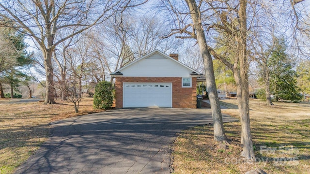 view of property exterior with brick siding, driveway, a chimney, and an attached garage