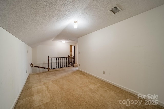 additional living space with carpet floors, visible vents, vaulted ceiling, a textured ceiling, and baseboards