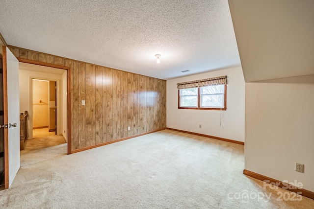 unfurnished room with a textured ceiling, wood walls, baseboards, and light colored carpet