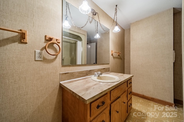 bathroom with baseboards, a shower with door, vanity, and wallpapered walls