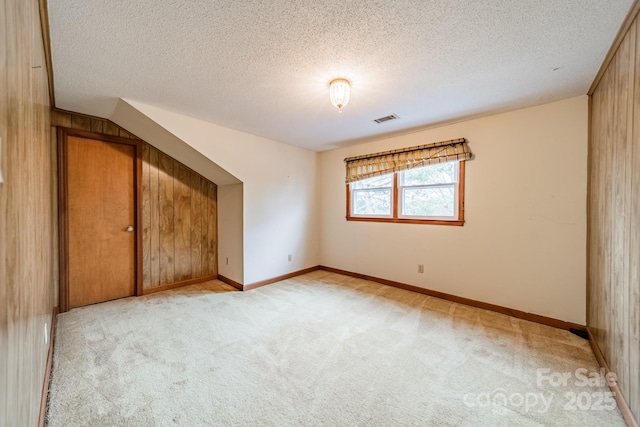 additional living space with light carpet, baseboards, visible vents, and a textured ceiling