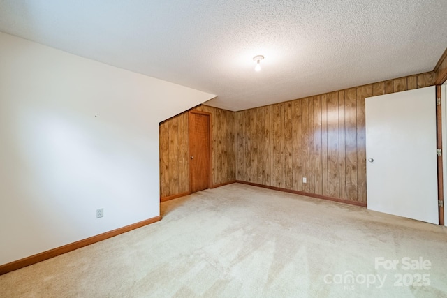 spare room with light carpet, wood walls, a textured ceiling, and baseboards