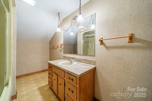 bathroom featuring lofted ceiling, vanity, baseboards, a shower with door, and wallpapered walls