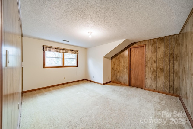 bonus room featuring light colored carpet, wood walls, a textured ceiling, and baseboards