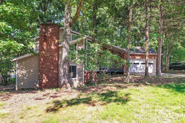 exterior space featuring a chimney, an attached garage, and a lawn