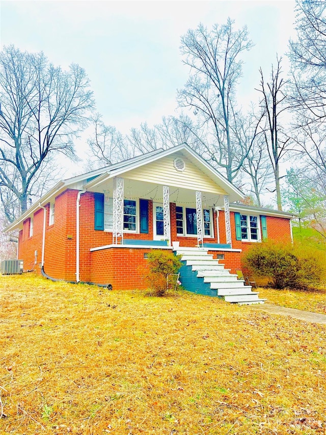 view of front facade featuring a front yard, central AC unit, a porch, and brick siding