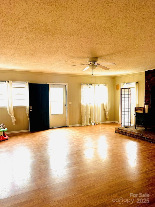 unfurnished living room with a wood stove, ceiling fan, a textured ceiling, and wood finished floors