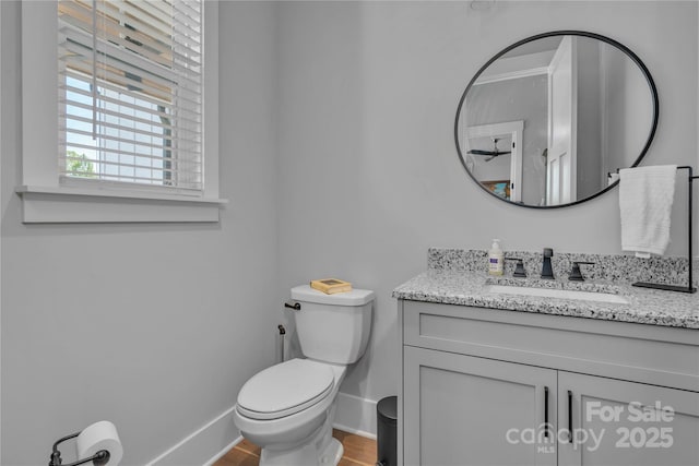 half bathroom with baseboards, vanity, and toilet