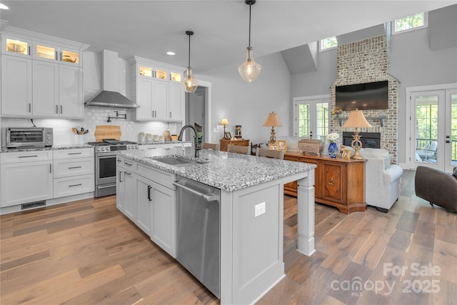 kitchen with stainless steel appliances, a fireplace, a sink, open floor plan, and wall chimney exhaust hood