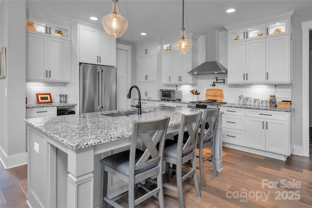 kitchen featuring white cabinets, a sink, wall chimney range hood, and high end refrigerator