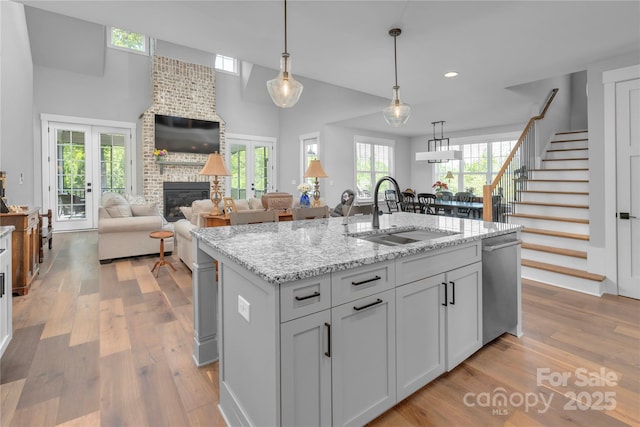 kitchen featuring french doors, light wood finished floors, stainless steel dishwasher, a brick fireplace, and a sink