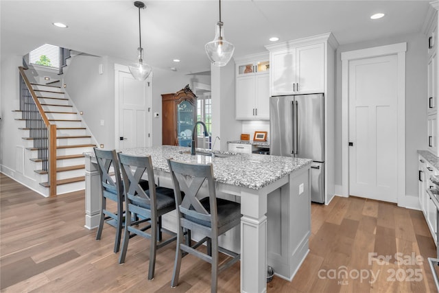 kitchen with high quality fridge, light wood-type flooring, a kitchen island with sink, and white cabinets