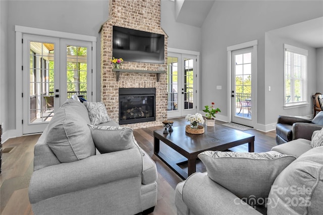 living area with french doors, a brick fireplace, wood finished floors, high vaulted ceiling, and baseboards