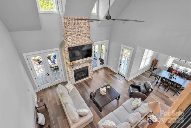 living room featuring wood finished floors, a towering ceiling, baseboards, french doors, and a brick fireplace