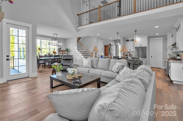 living area featuring recessed lighting, wood finished floors, a towering ceiling, baseboards, and stairway