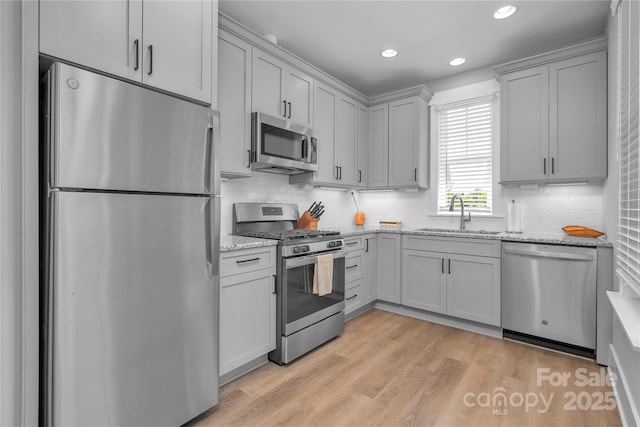 kitchen featuring tasteful backsplash, appliances with stainless steel finishes, light stone countertops, light wood-style floors, and a sink