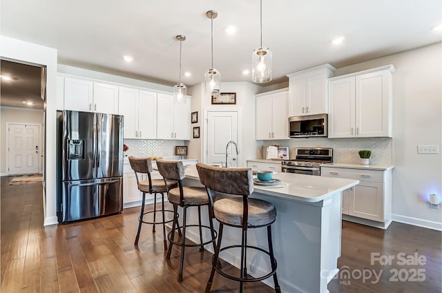 kitchen with pendant lighting, light countertops, appliances with stainless steel finishes, white cabinets, and a kitchen island with sink