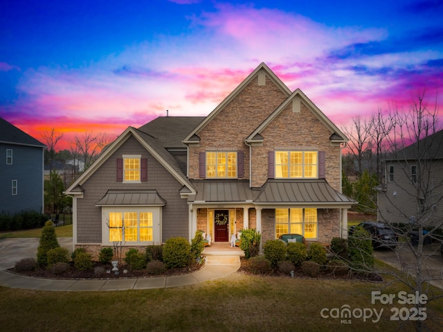 craftsman-style home featuring a porch, a lawn, a standing seam roof, metal roof, and stone siding