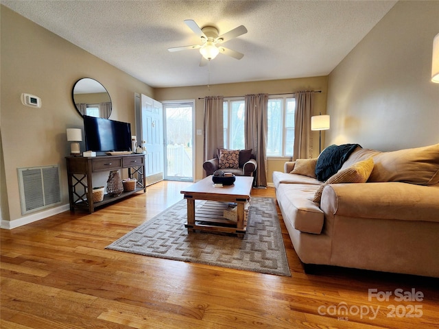 living room with ceiling fan, a textured ceiling, and light wood-type flooring