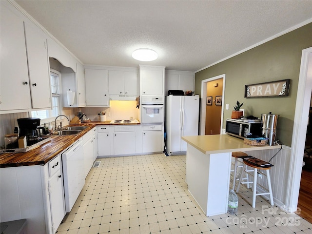 kitchen with a breakfast bar, white cabinetry, sink, ornamental molding, and white appliances