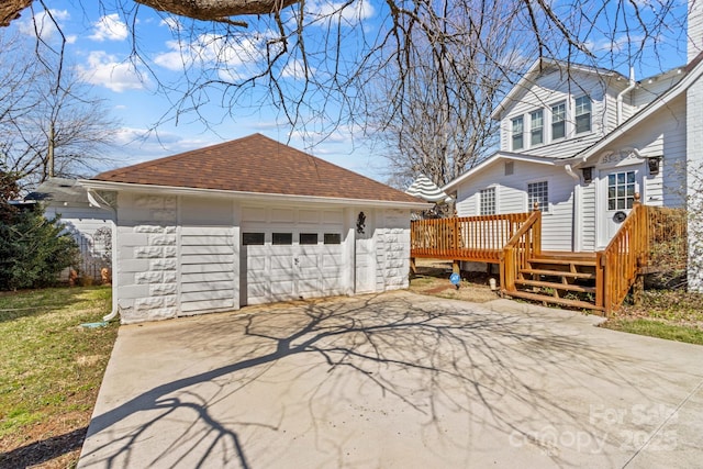 view of side of property featuring a deck, a garage, a shingled roof, an outdoor structure, and driveway