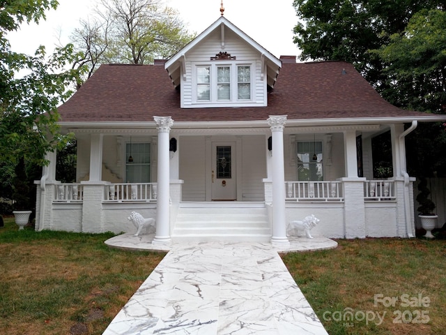 view of front of property featuring covered porch, roof with shingles, and a front lawn