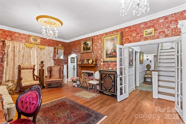 living area with wallpapered walls, a chandelier, wood finished floors, and ornamental molding