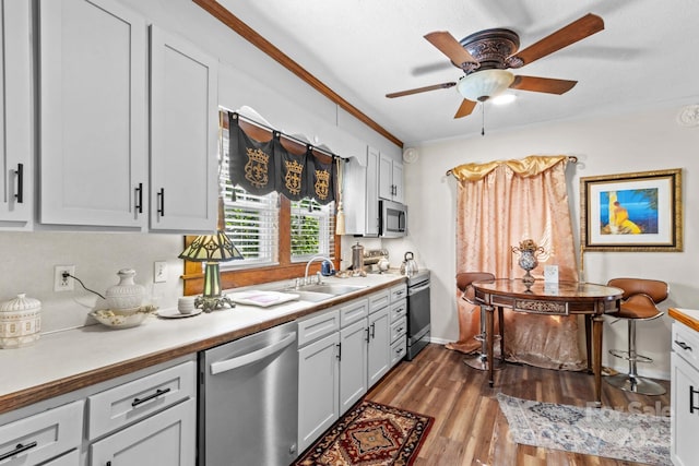 kitchen with ornamental molding, stainless steel appliances, light countertops, light wood-type flooring, and a sink