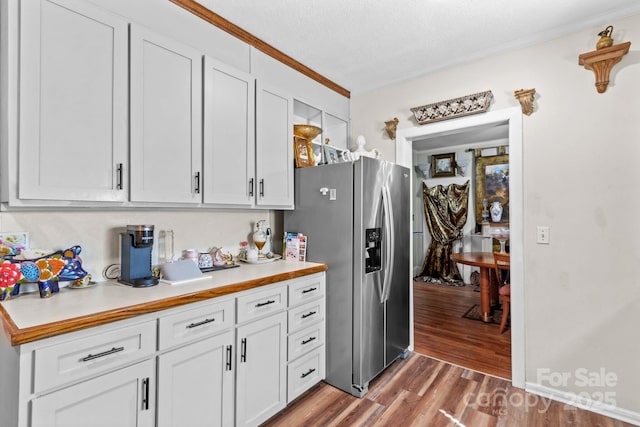 kitchen with wood finished floors, white cabinetry, light countertops, ornamental molding, and stainless steel refrigerator with ice dispenser