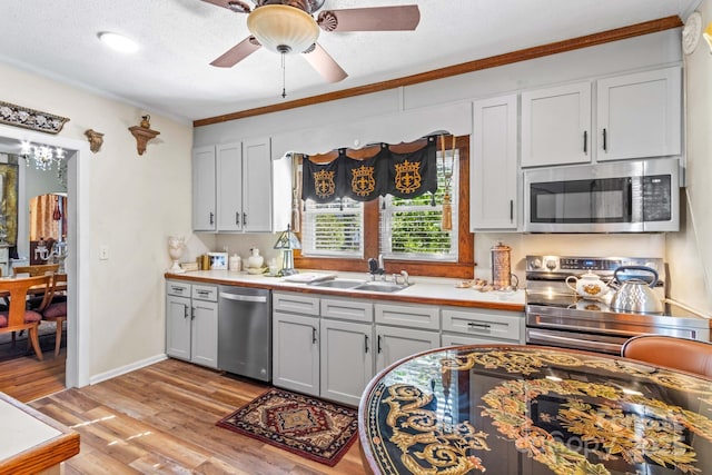 kitchen featuring light wood finished floors, stainless steel appliances, crown molding, light countertops, and a sink