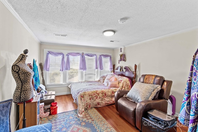 bedroom featuring visible vents, ornamental molding, a textured ceiling, wood finished floors, and baseboards