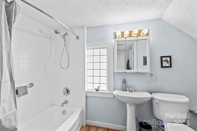 bathroom featuring baseboards, toilet, wood finished floors, vaulted ceiling, and shower / bathing tub combination