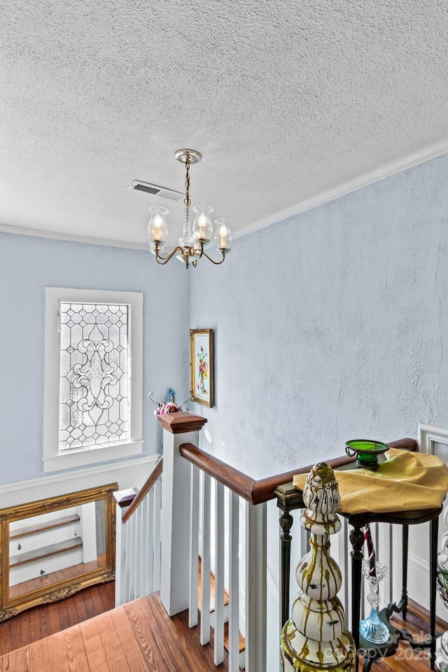 staircase featuring a chandelier, a textured wall, a textured ceiling, wood finished floors, and visible vents