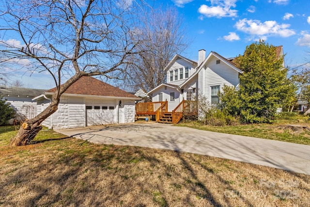 view of front facade featuring a chimney, a front yard, a deck, driveway, and an outdoor structure