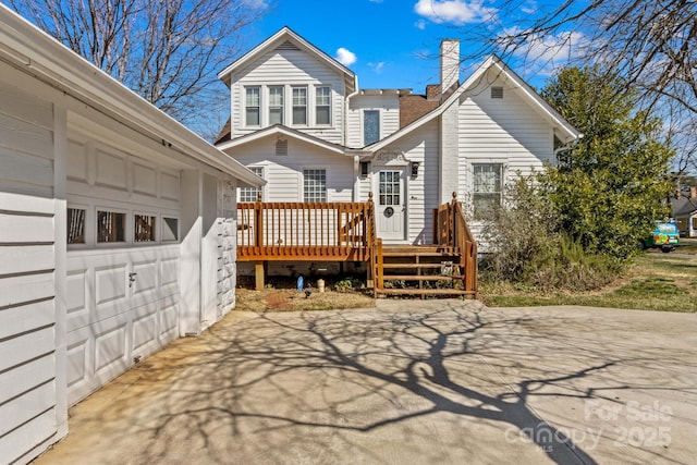 rear view of house featuring driveway, a chimney, and a wooden deck