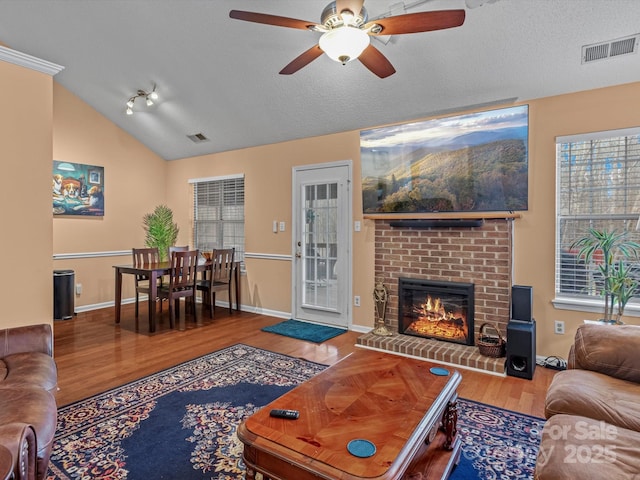 living room featuring lofted ceiling, a brick fireplace, a textured ceiling, hardwood / wood-style flooring, and ceiling fan