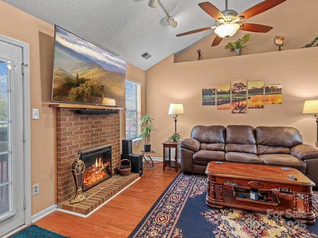 living room with hardwood / wood-style flooring, a brick fireplace, vaulted ceiling, and a textured ceiling