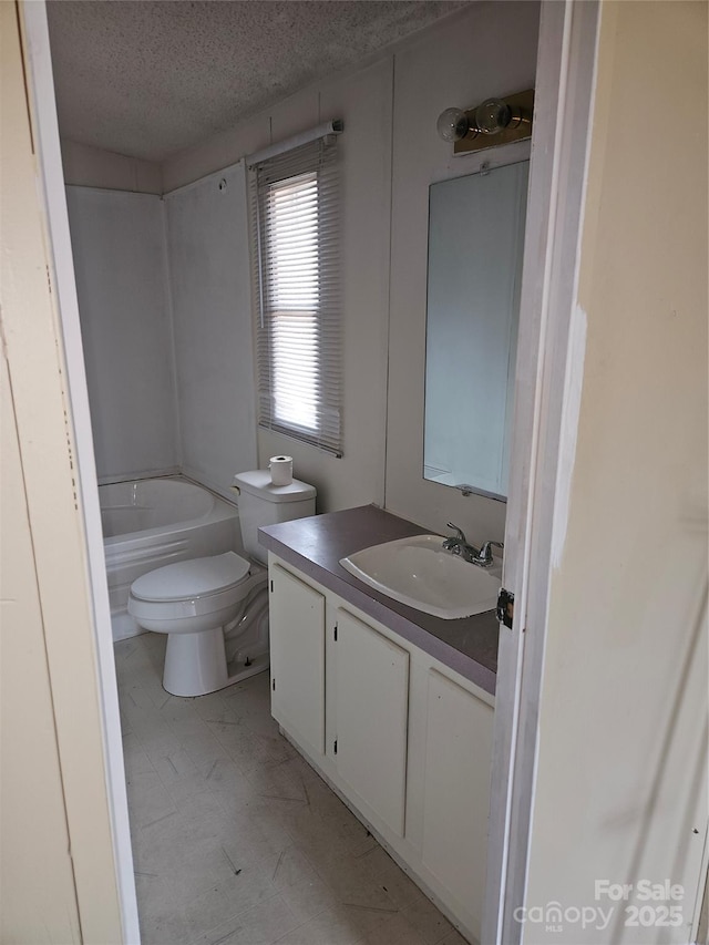 bathroom featuring a washtub, vanity, toilet, and a textured ceiling