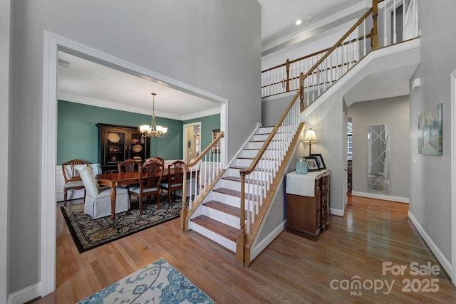 staircase featuring a towering ceiling, hardwood / wood-style flooring, crown molding, and a chandelier