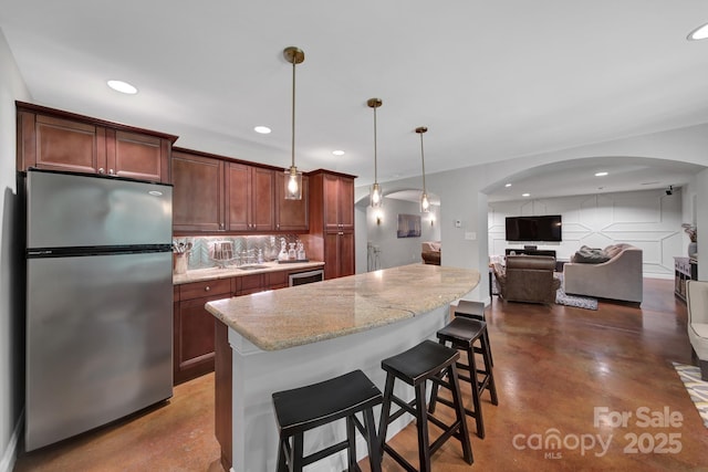 kitchen with hanging light fixtures, light stone counters, a breakfast bar, stainless steel fridge, and backsplash