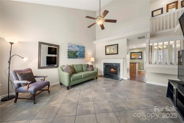 living room with ceiling fan with notable chandelier, a towering ceiling, a fireplace, and tile patterned flooring