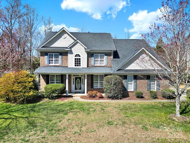 traditional-style house featuring a front yard, brick siding, and a shingled roof